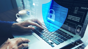 Person typing on a laptop with a transparent digital shield and lock icon overlay, representing cybersecurity, data protection, and secure online access.