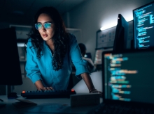Cybersecurity professional analyzing code on multiple monitors in a modern security operations center, investigating threats and system defenses.