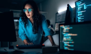 Cybersecurity professional analyzing code on multiple monitors in a modern security operations center, investigating threats and system defenses.