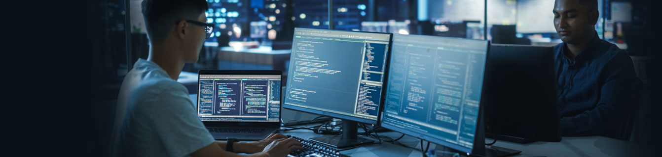 Junger Mann mit Brille arbeitet vor 3 Monitoren