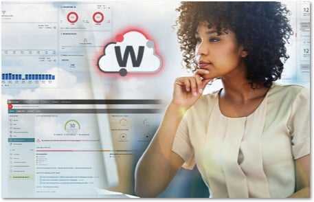 Black woman with natural curly hair in a white silk top looking at a monitor with WatchGuard Cloud screens behind her