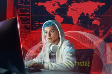 Eine Person mit blauen Haaren in einem weißen Hoodie mit Kopfhörern schaut auf einen Monitor.