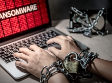 Hands chained with a padlock typing on a laptop showing a ransomware attack warning; symbolizing data encryption and cyber extortion.