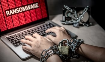 Hands chained with a padlock typing on a laptop showing a ransomware attack warning; symbolizing data encryption and cyber extortion.