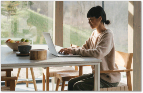 Woman in white sweater sitting in an airy dining room on her laptop